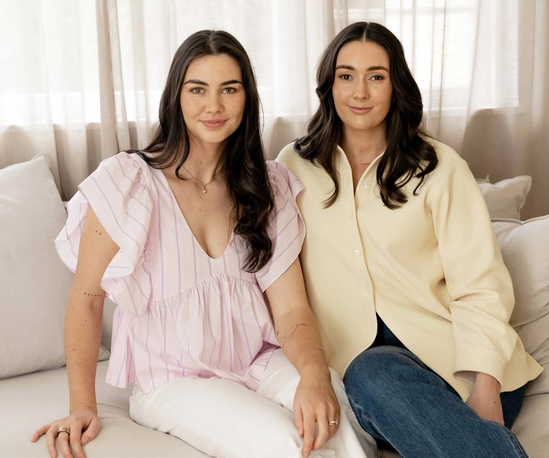 Two woman sitting on couch, one in pink and other in yellow