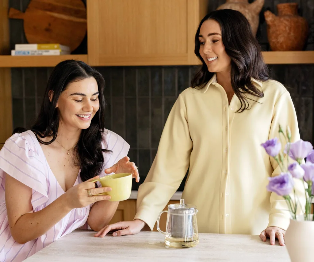 two woman in kitchen drinking a cup o ftea