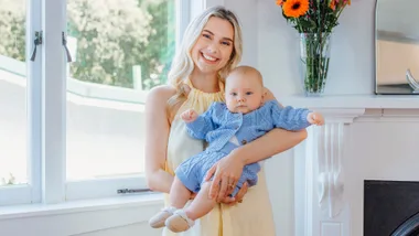 Caitlin Crisp in yellow dress holding baby charlie in a blue knit set