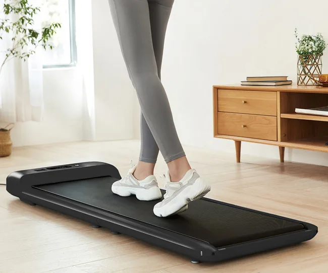 Woman in grey leggings walking on a walking pad in the lounge