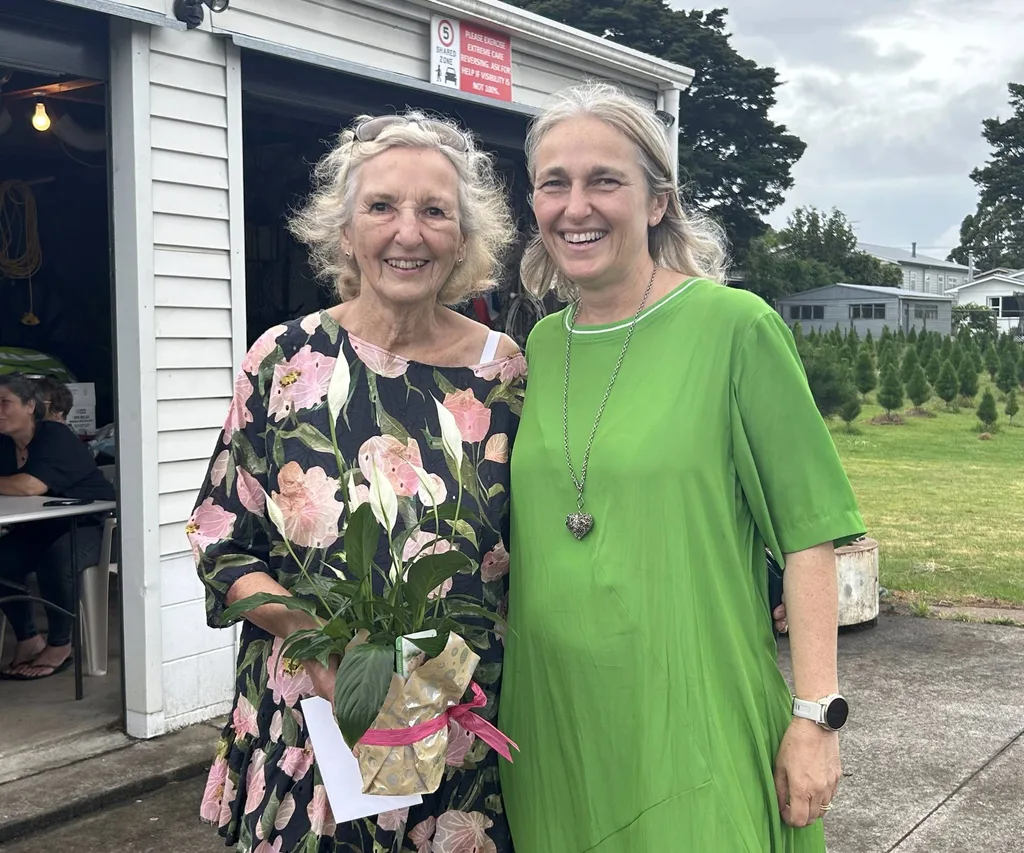two woman smiling holding plant and in green