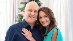 Man in blue shirt and woman in blue dress smiling in front of Christmas tree