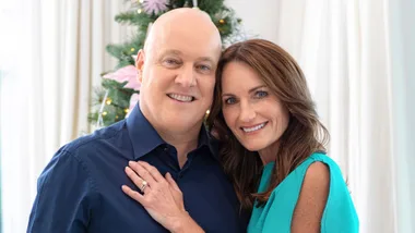 Man in blue shirt and woman in blue dress smiling in front of Christmas tree