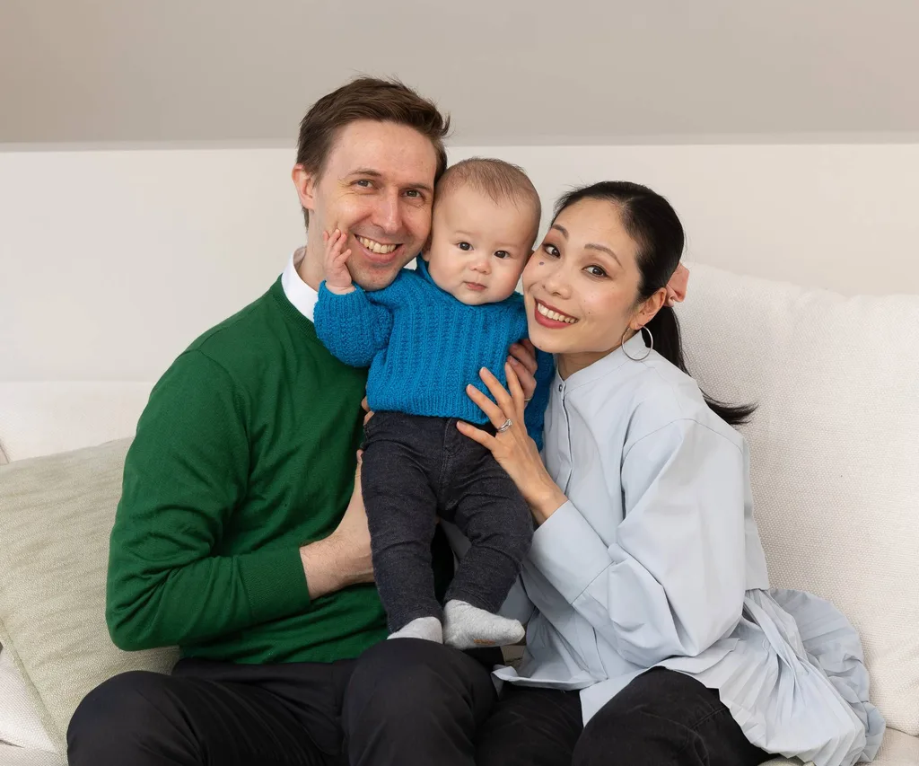 Woman and man holding baby in the middle of them sitting on the couch