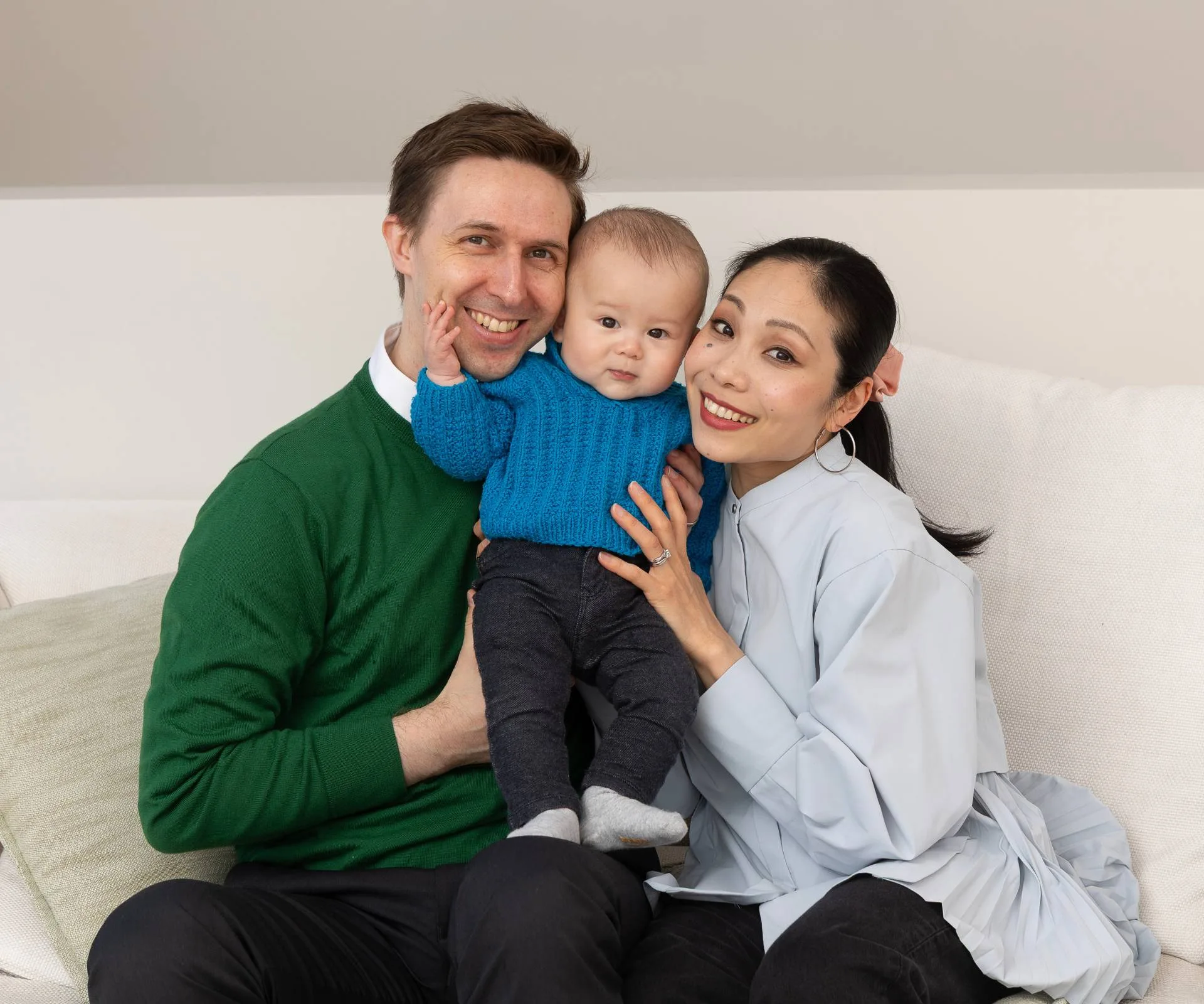 Woman and man holding baby in the middle of them sitting on the couch