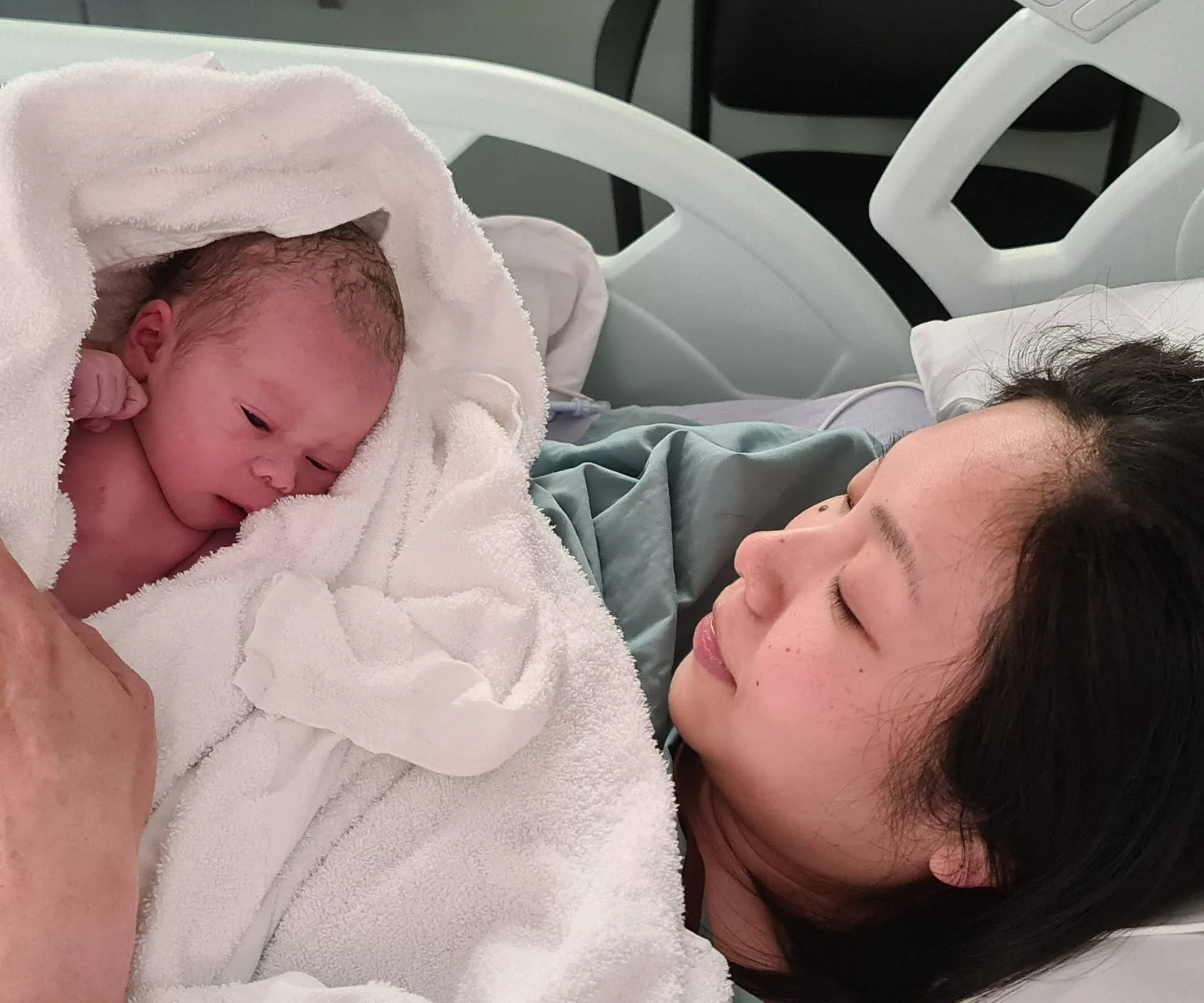 Woman giving holding new born baby in hospital bed