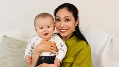Woman in green top holding baby in dog pattern shirt sitting on couch
