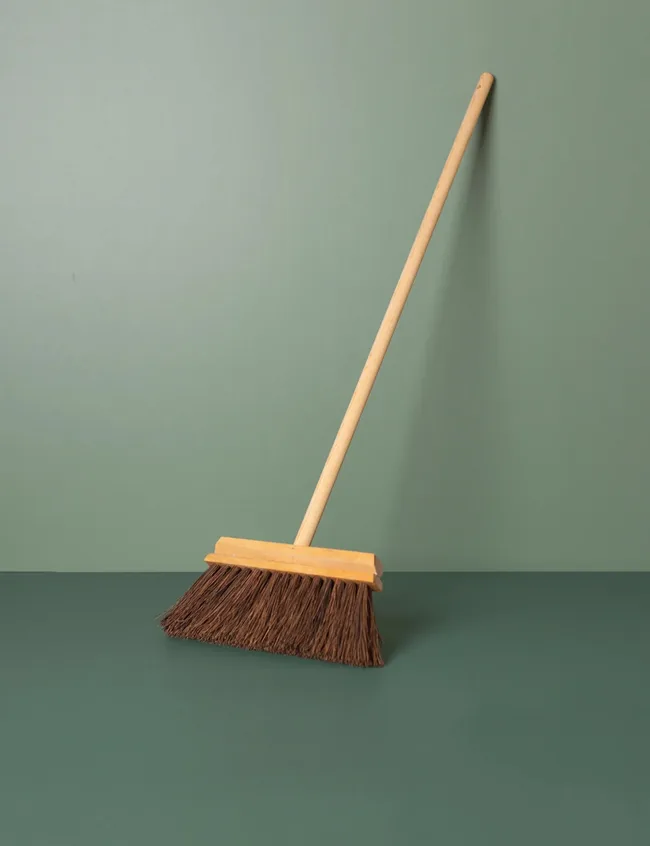 Long-handled wooden broom with dark brown bristles, propped against green background