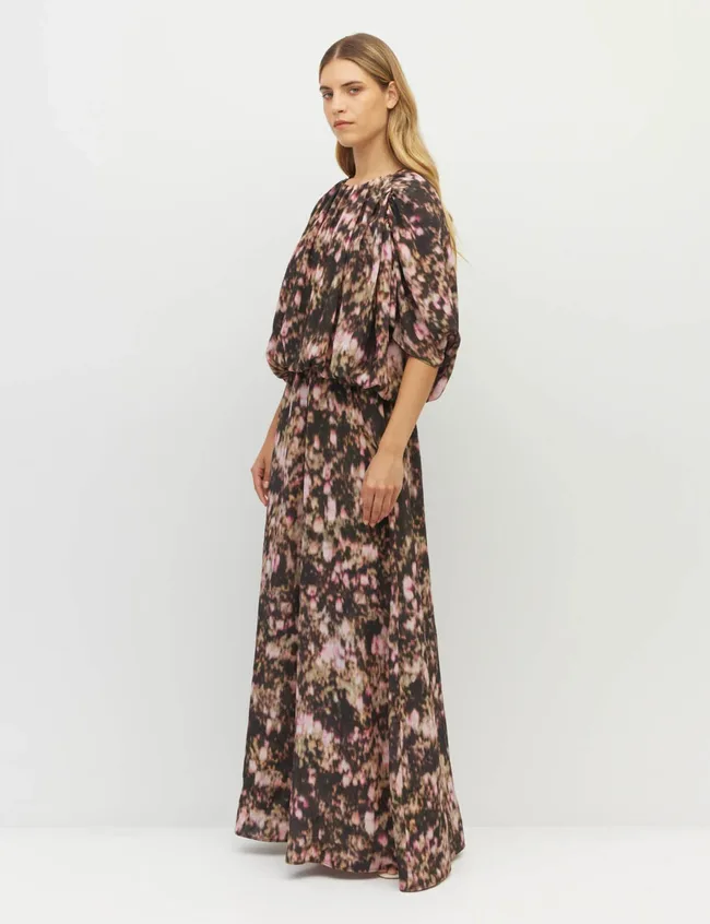 Woman wearing floor-length dress featuring abstract floral print in shades of green, pink, dark purple and brown