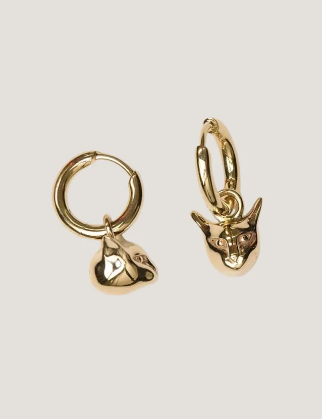 Small gold sleeper-style earrings with cat charms on a grey background