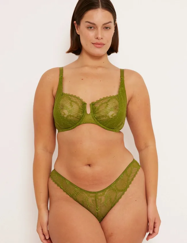 Woman standing against grey background, wearing green lace bra and briefs