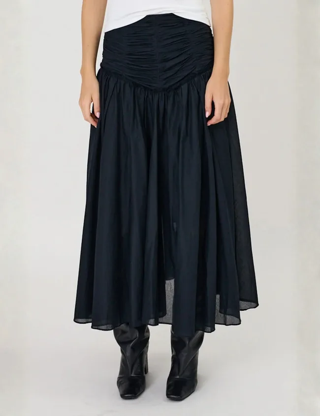 Close crop of woman from waist down, wearing ankle length black skirt and black boots