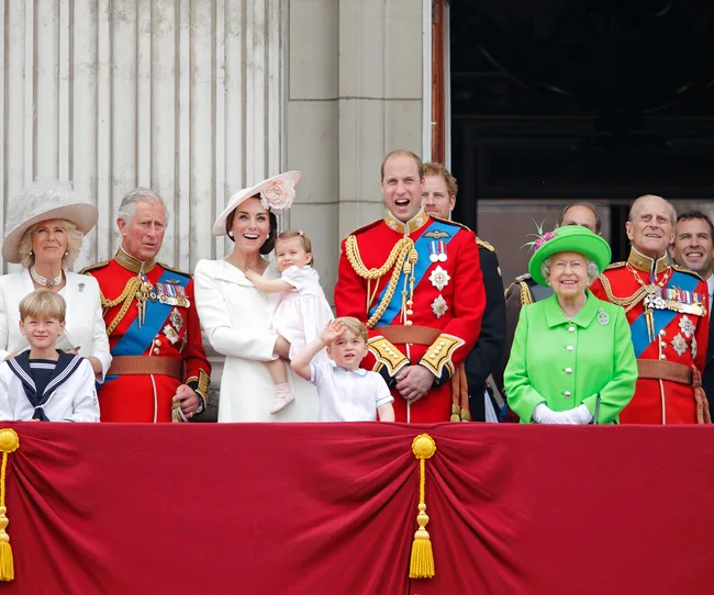 A group of royals on a balcony during a formal event, featuring military uniforms and elegant attire.