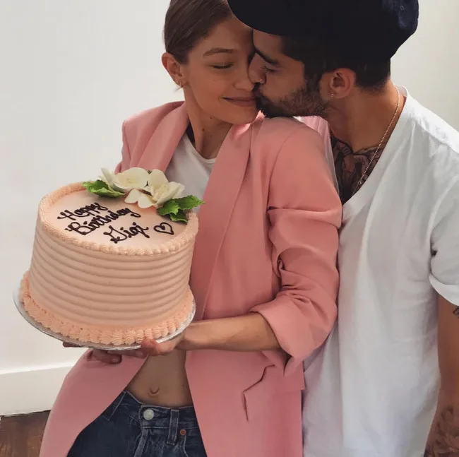 A person holding a birthday cake while being kissed on the cheek by another person.