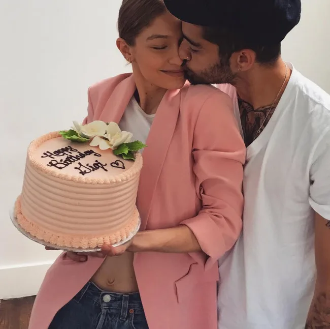 A person holding a birthday cake while being kissed on the cheek by another person.
