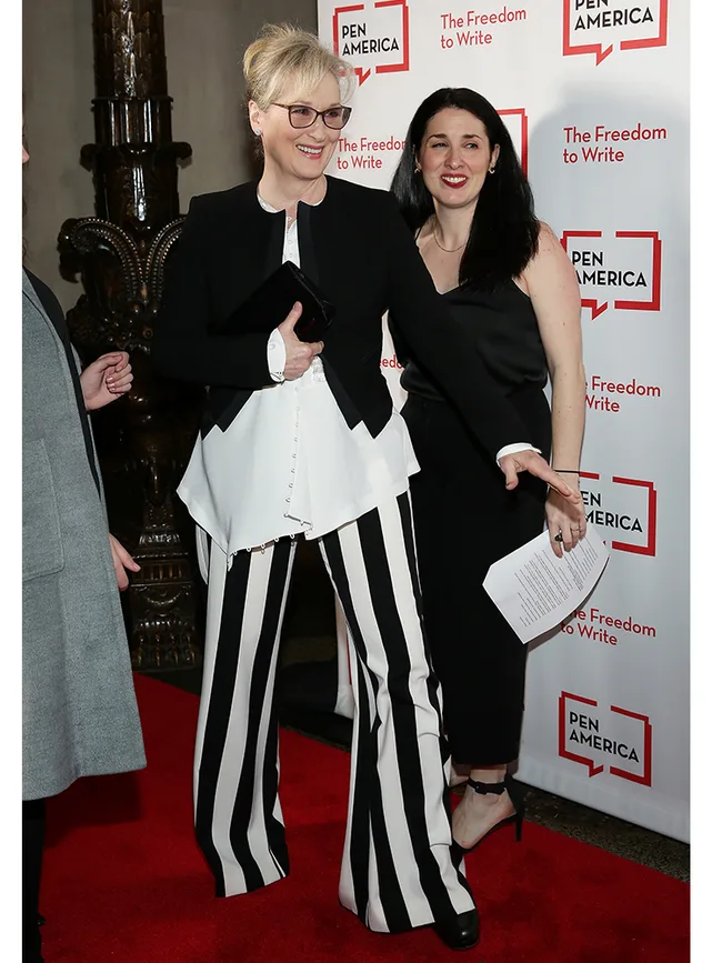 Two women on the red carpet at a PEN America event. One wears striped pants, the other holds papers.