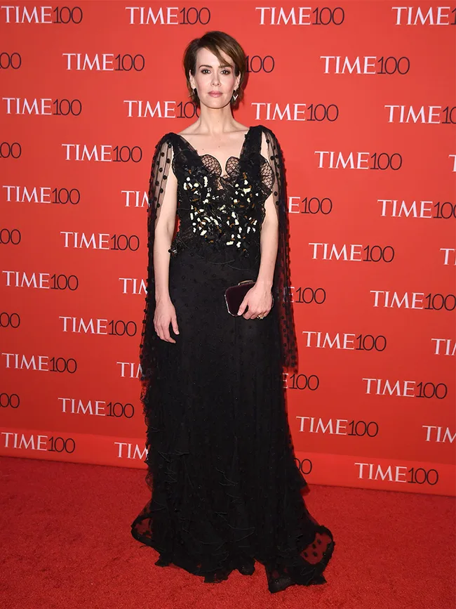 Person in an elegant black gown on the red carpet at the TIME 100 event, standing in front of the step-and-repeat backdrop.