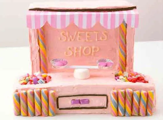 Sweet shop-themed cake with pink icing, striped canopy, and colorful candy decorations.