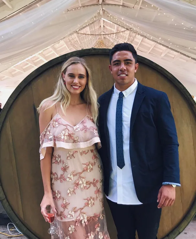 A man in a suit and a woman in a floral dress pose in front of a large wine barrel at an indoor event.