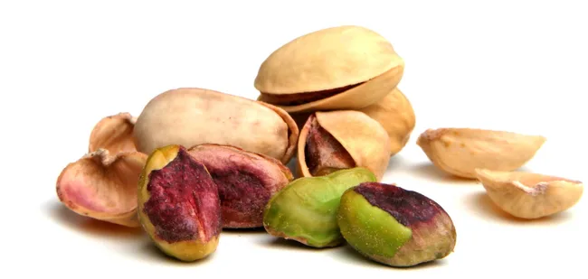 Close-up of pistachios with shells, showing green and purple kernels on a white background.
