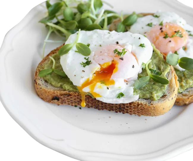 Avocado toast topped with poached eggs, garnished with microgreens on a white plate.
