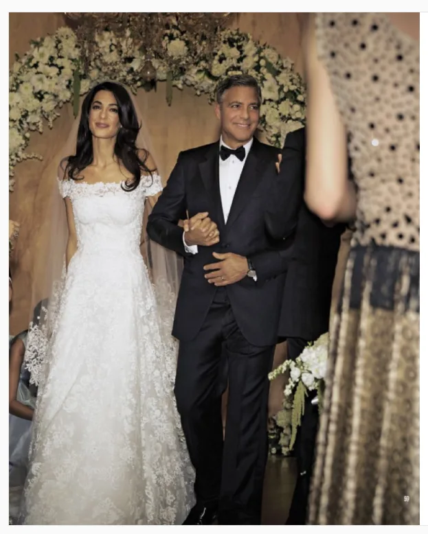 A couple in wedding attire, the bride in a white lace gown and the groom in a black tuxedo, smiling and walking together.