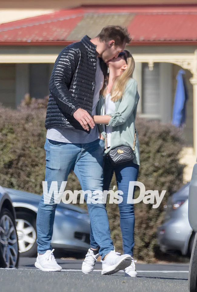 A couple shares a kiss on a street, with cars in the background and the Woman's Day logo on the image.