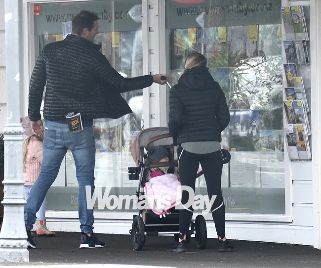 A man and a woman with a stroller and a child outside a real estate office, viewed from the back.