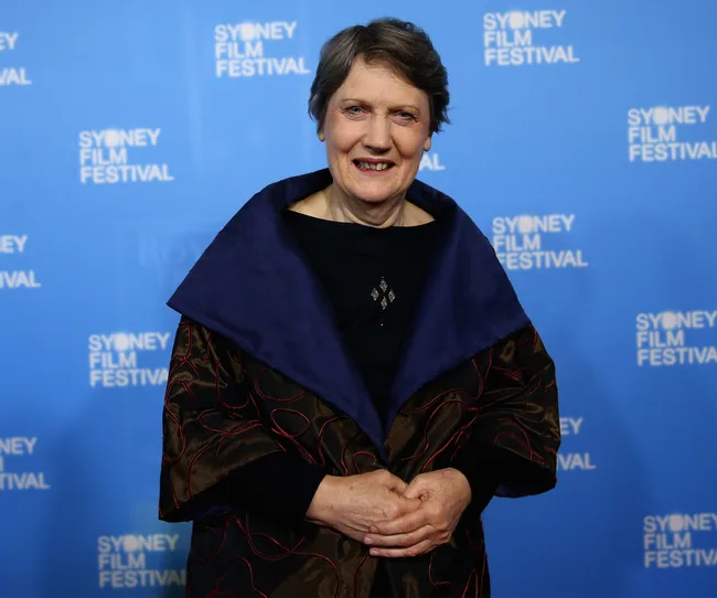 A person smiling at the Sydney Film Festival, wearing a dark outfit with a patterned coat.