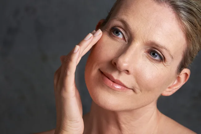 Middle-aged woman touching her cheek gently, with a thoughtful expression against a dark background.