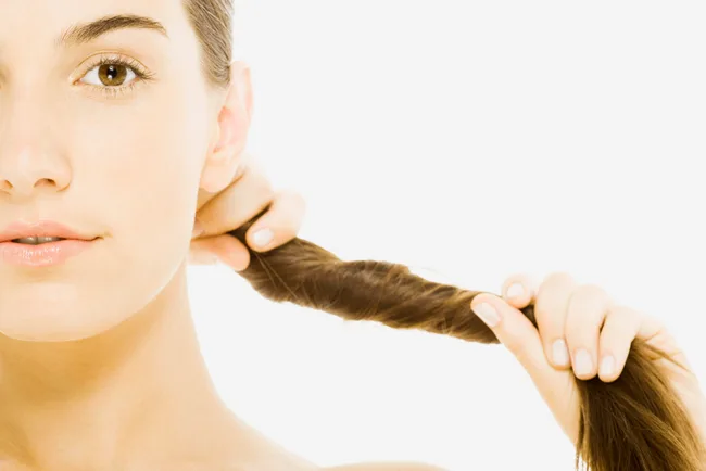 Close-up of a woman pulling her brown hair to one side, showing half of her face with neutral expression.