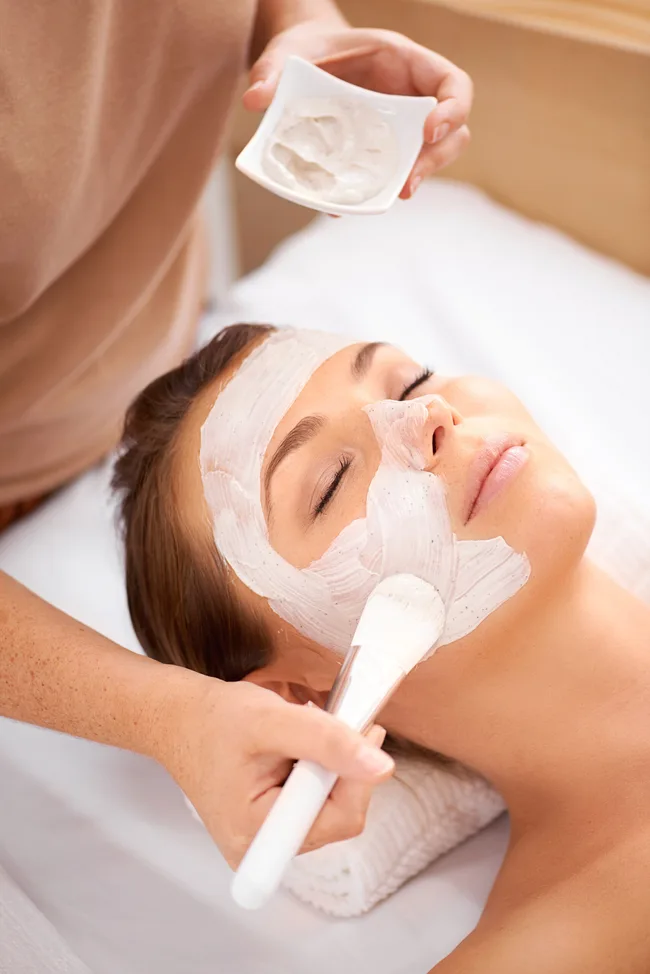 A person receiving a facial mask application with a brush at a spa.