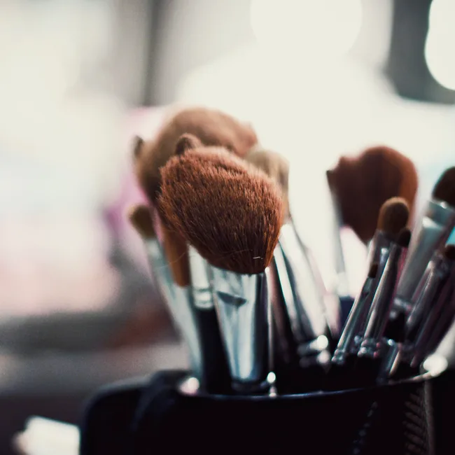 A close-up of several makeup brushes in a holder, with soft lighting in the background.