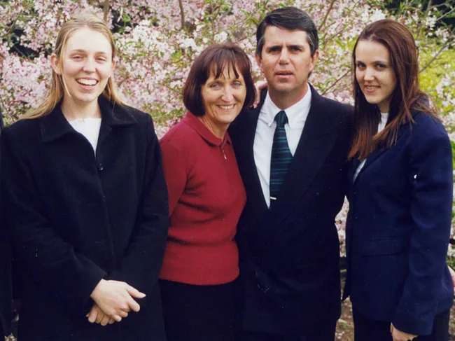 A group of four people standing outdoors with blooming trees in the background.