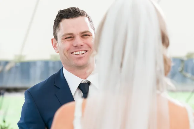 Man in a blue suit smiling at a bride during a wedding ceremony.