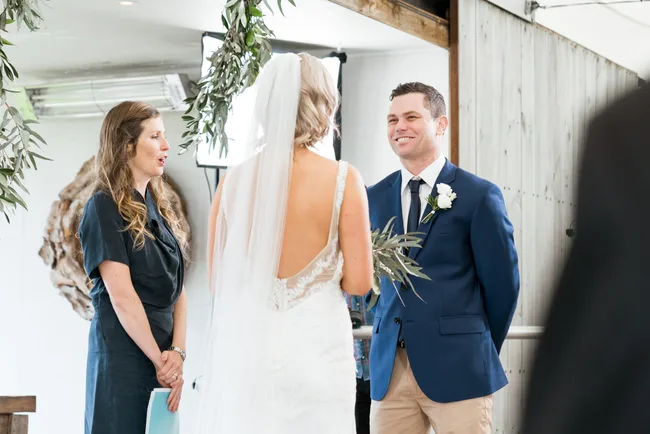 Wedding ceremony with a bride, groom in a blue suit, and an officiant indoors.