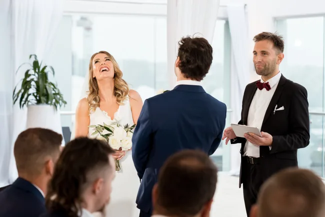 Bride laughing during a wedding ceremony with groom and officiant present.