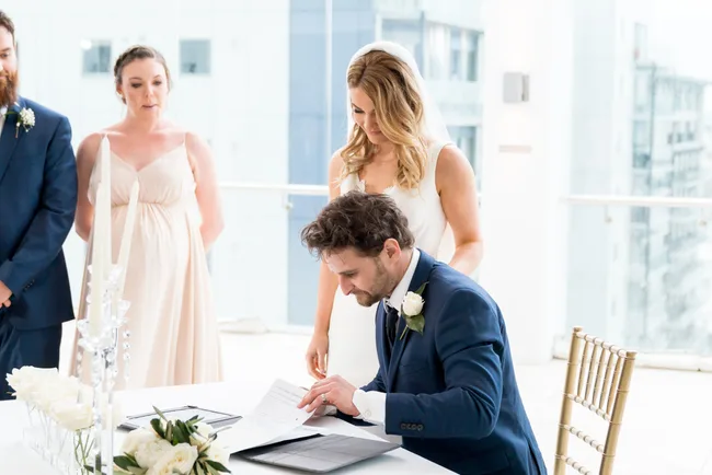 Bride and groom signing marriage certificate at a wedding ceremony indoors.
