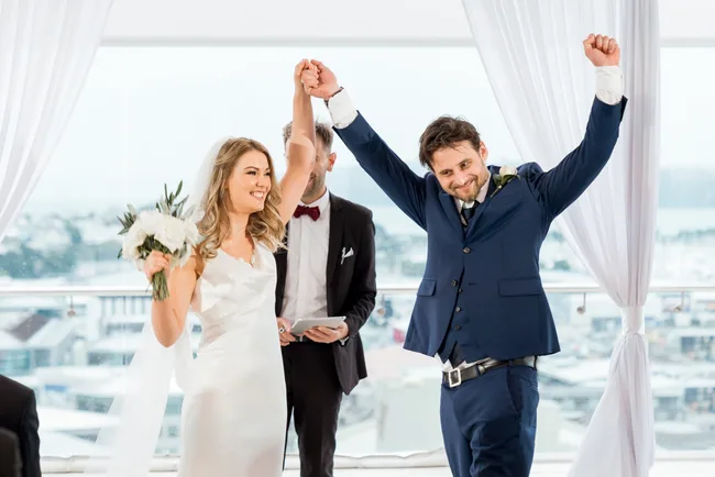 Newlywed couple celebrating with raised arms at their wedding ceremony indoors.