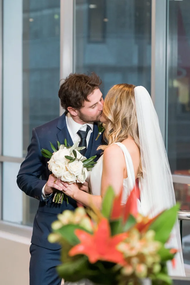 Bride and groom kissing indoors, the bride holds a white rose bouquet.
