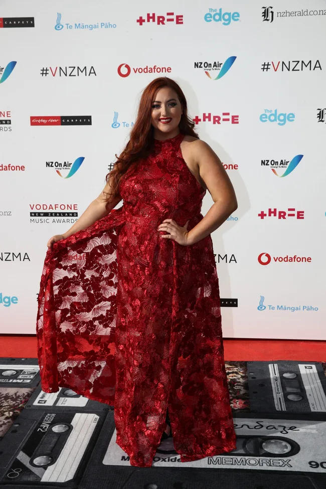 Person in a red lace gown poses on the Vodafone New Zealand Music Awards red carpet.