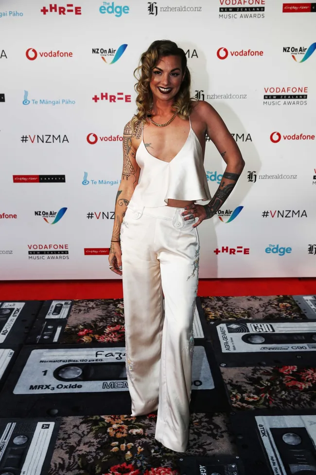 A person in a white outfit poses on the red carpet at the Vodafone New Zealand Music Awards.