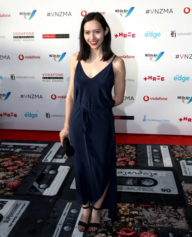 Young woman in a navy dress on a music awards red carpet with a cassette tape pattern underfoot.