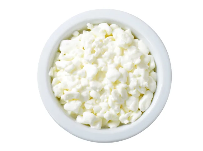 White bowl filled with cottage cheese on a white background.