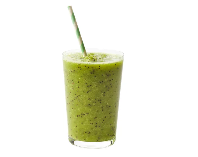A tall glass of green kiwi smoothie with a striped straw.
