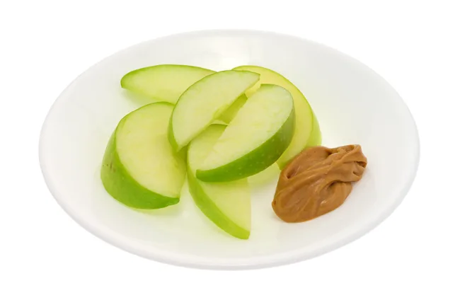 Sliced green apple on a white plate with a dollop of peanut butter.
