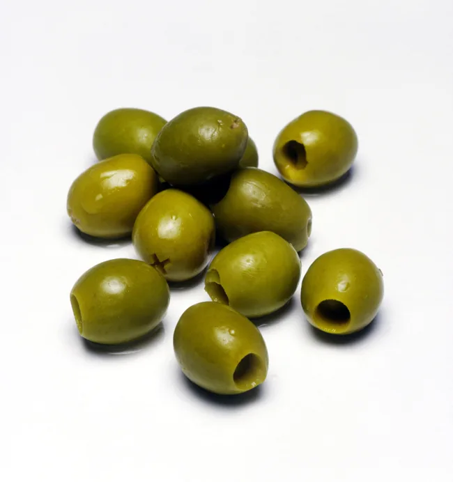 Pitted green olives scattered on a white surface.