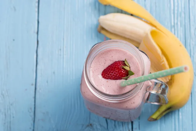 Strawberry banana smoothie in a jar with straw on blue wooden table.