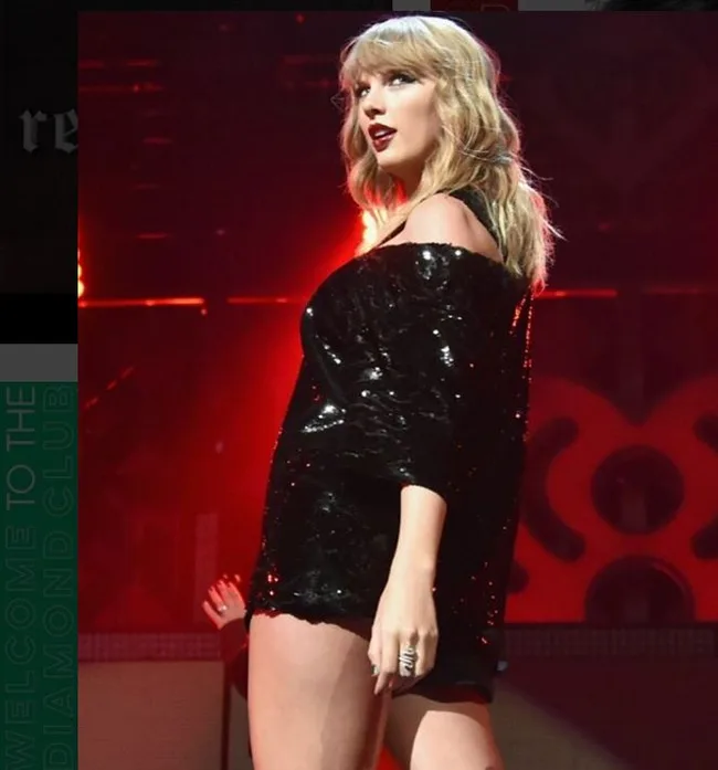 A person in a black sequined dress performs on stage with red lighting in the background.