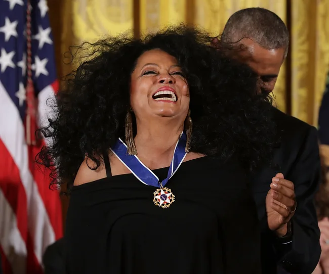 A person receives a medal at an event, smiling widely, with an American flag in the background.